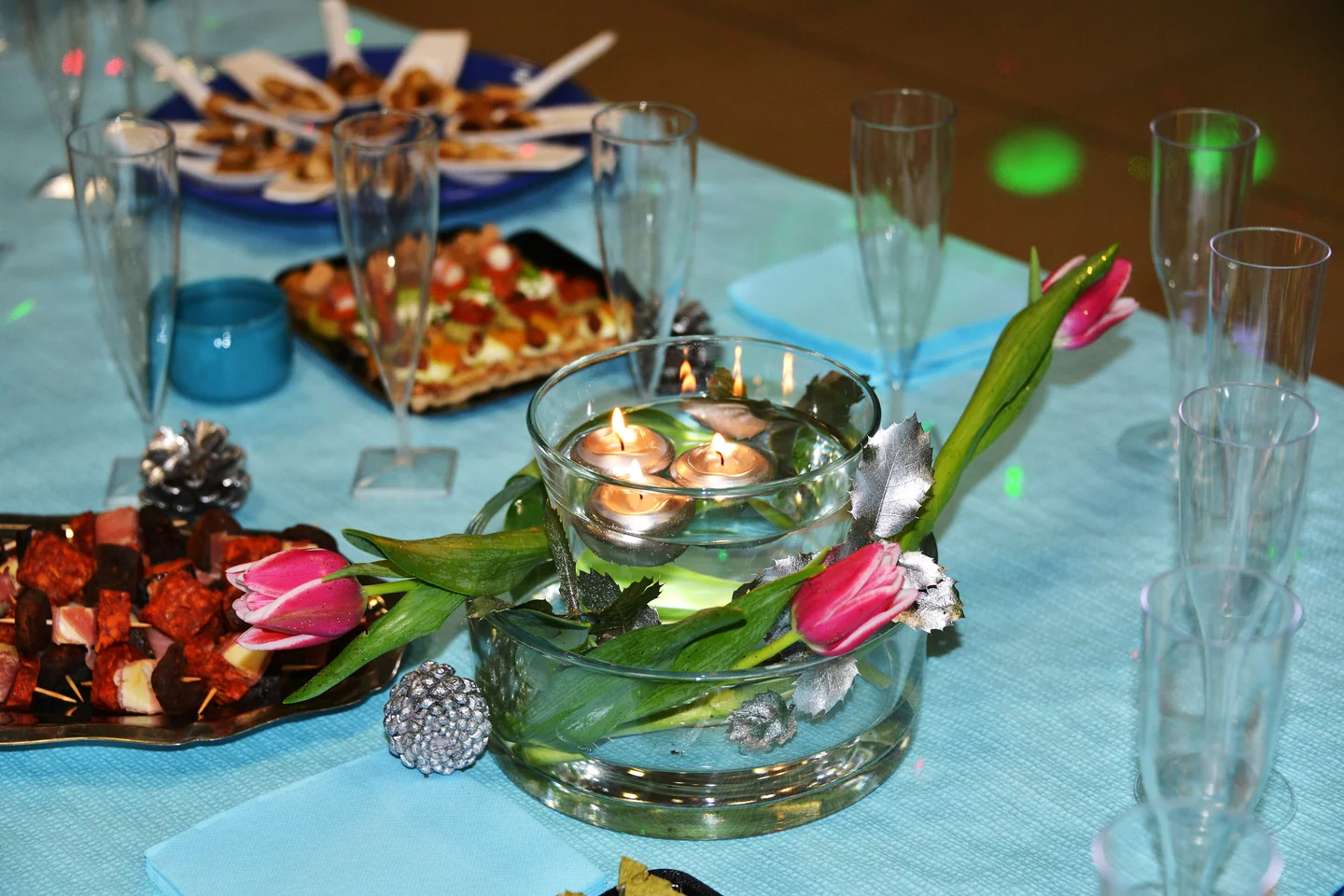 Photophore en verre avec bougies flottantes et tulipes roses sur nappe turquoise