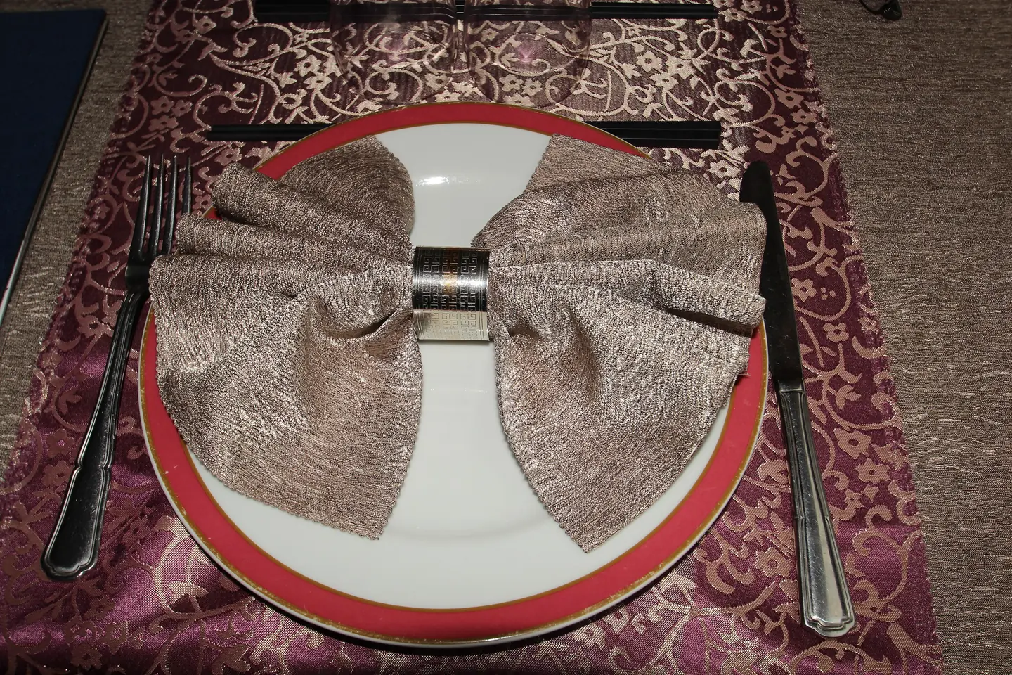 Serviette en nœud papillon sur assiette, sur un chemin de table damassé
