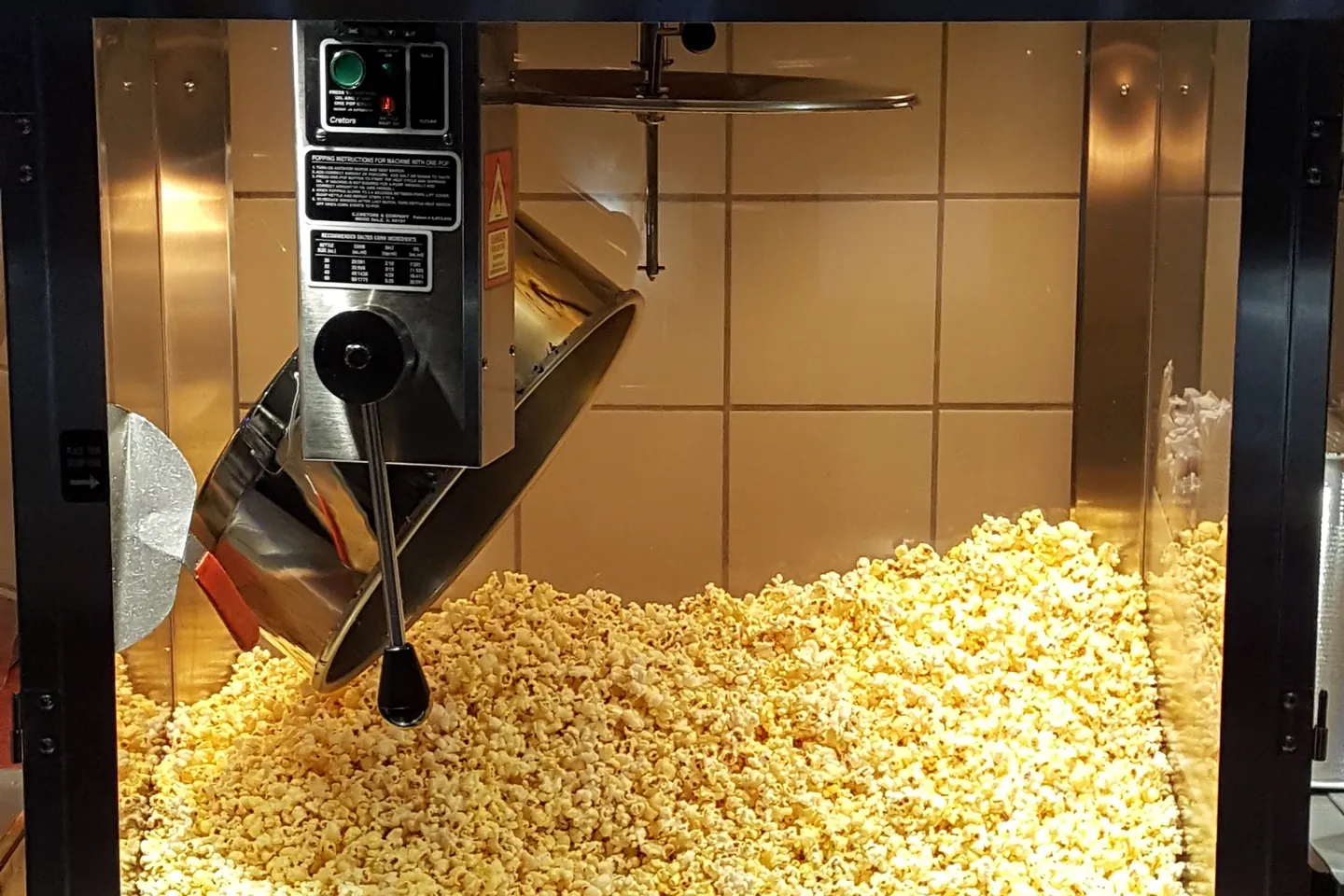 Machine à pop-corn vitrée et lumineuse, marmite inox au-dessus d’un tas de pop-corn doré tout juste éclaté